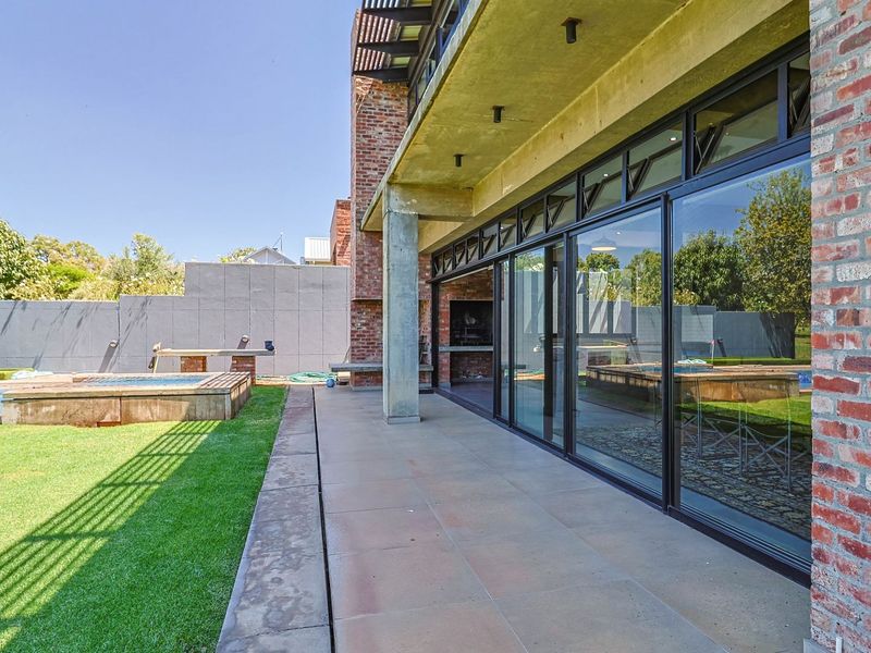 Spacious covered patio featuring exposed brickwork, concrete columns, and large sliding glass doors, seamlessly connecting the indoor living area to the garden and pool.