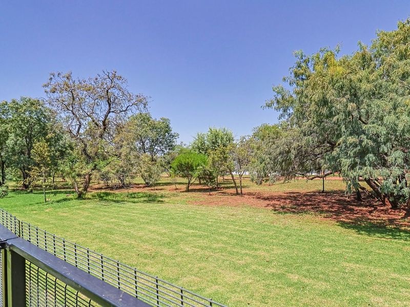 A spacious, well-maintained garden area featuring established trees, a manicured lawn, and secure perimeter fencing.