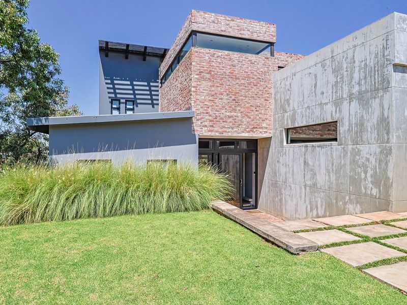 Modern architectural home featuring a striking combination of exposed brick and concrete finishes, complemented by a well-maintained lawn and paved entrance.