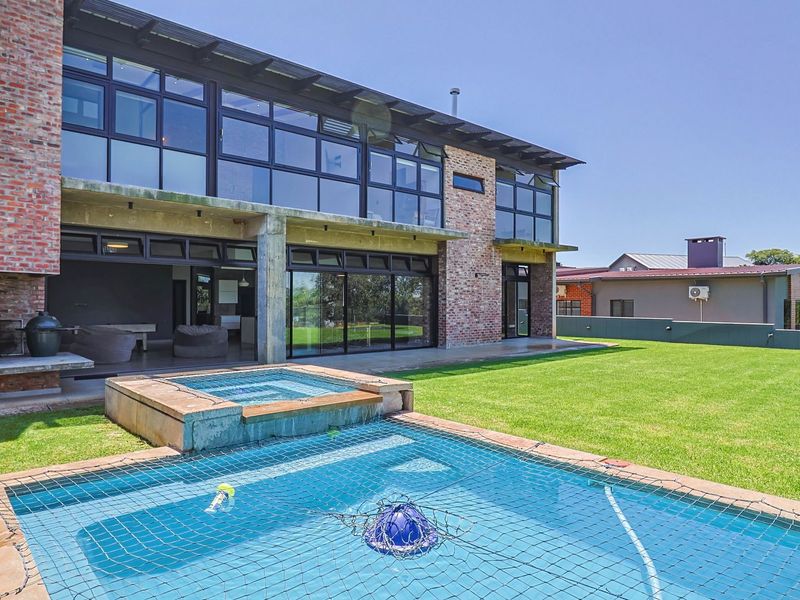 Rear view of a modern two-story home featuring extensive glass paneling, a brick facade, an outdoor fireplace, and a swimming pool with a raised spa.