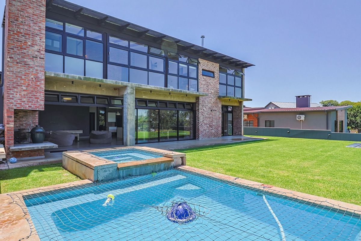 Rear view of a modern two-story home featuring extensive glass paneling, a brick facade, an outdoor fireplace, and a swimming pool with a raised spa.