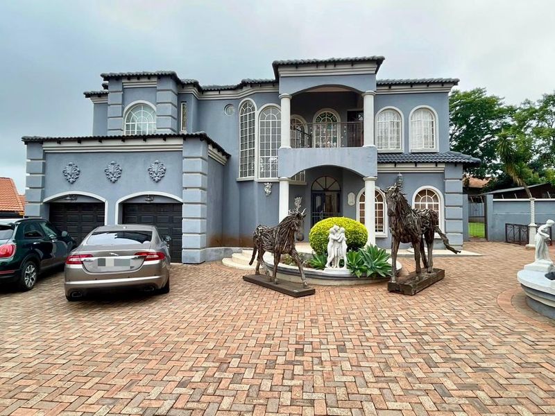 A grand double-story residence featuring a paved driveway, double garage, arched architectural detailing, and a prominent front balcony.