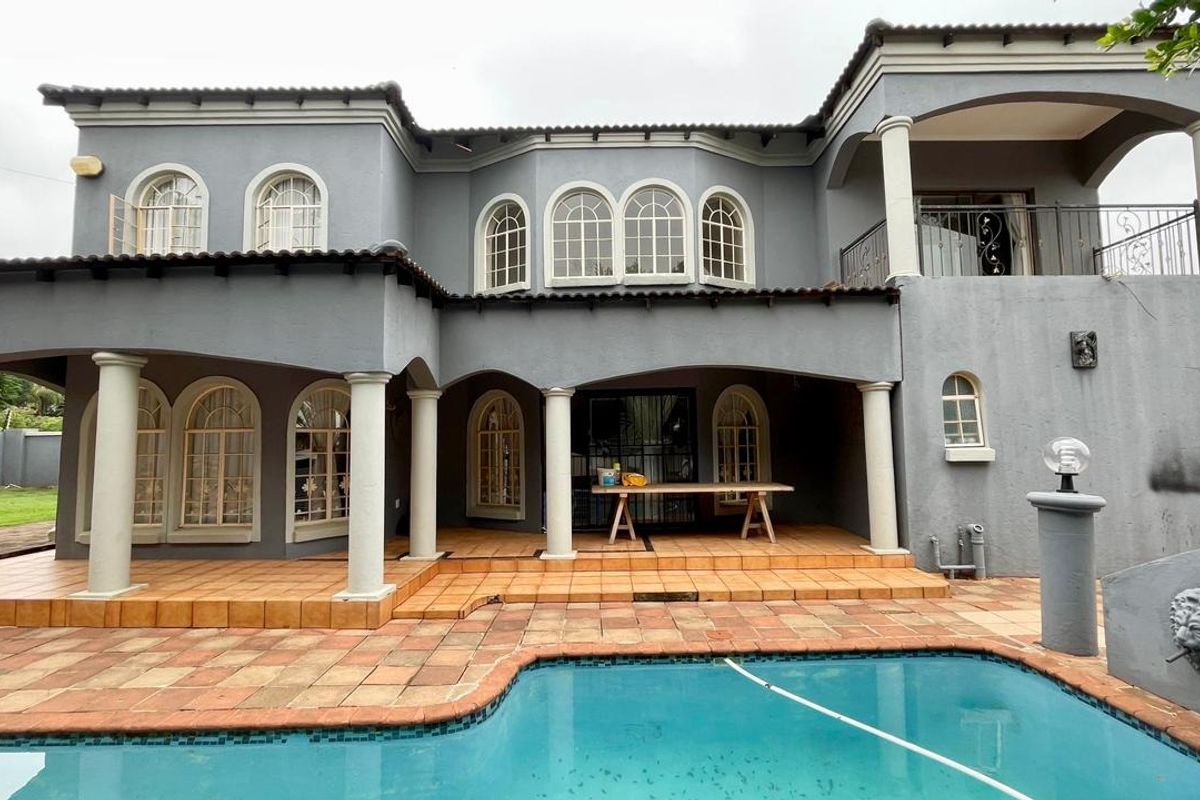 Rear view of a two-story home featuring a covered patio, upper balcony, arched windows, and a swimming pool with tiled surround.