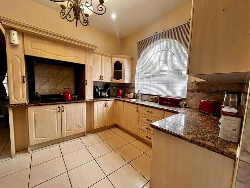 A functional kitchen featuring light wood cabinetry, granite countertops, tiled flooring, and a distinctive arched window, offering a classic layout with ample storage space.