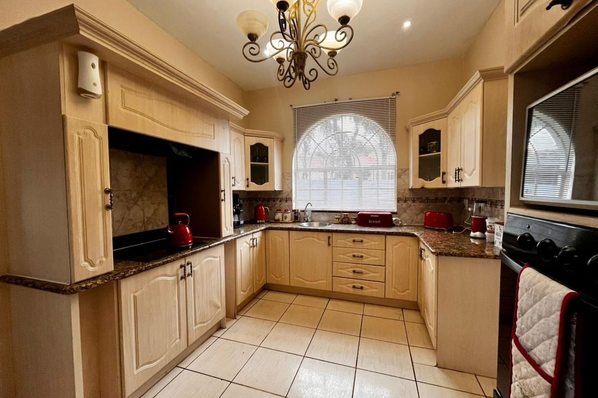A traditional kitchen featuring light wood cabinetry, granite countertops, ceramic tile flooring, and a distinctive arched window, providing a functional and classic cooking space.