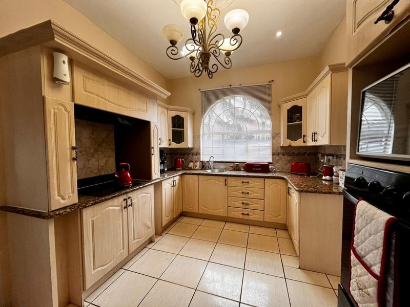 A traditional kitchen featuring light wood cabinetry, granite countertops, ceramic tile flooring, and a distinctive arched window, providing a functional and classic cooking space.