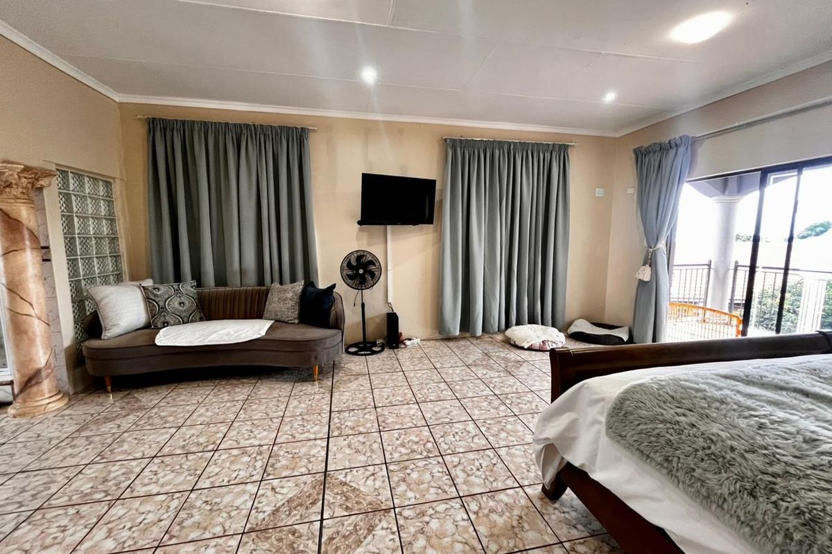 Spacious bedroom featuring tiled flooring, recessed lighting, and a glass block accent wall, with direct access to an outdoor balcony area.