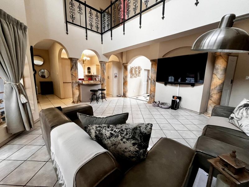 Spacious open-plan living area featuring decorative columns, arched architectural details, a mezzanine level with wrought iron railing, and neutral tiled flooring throughout.