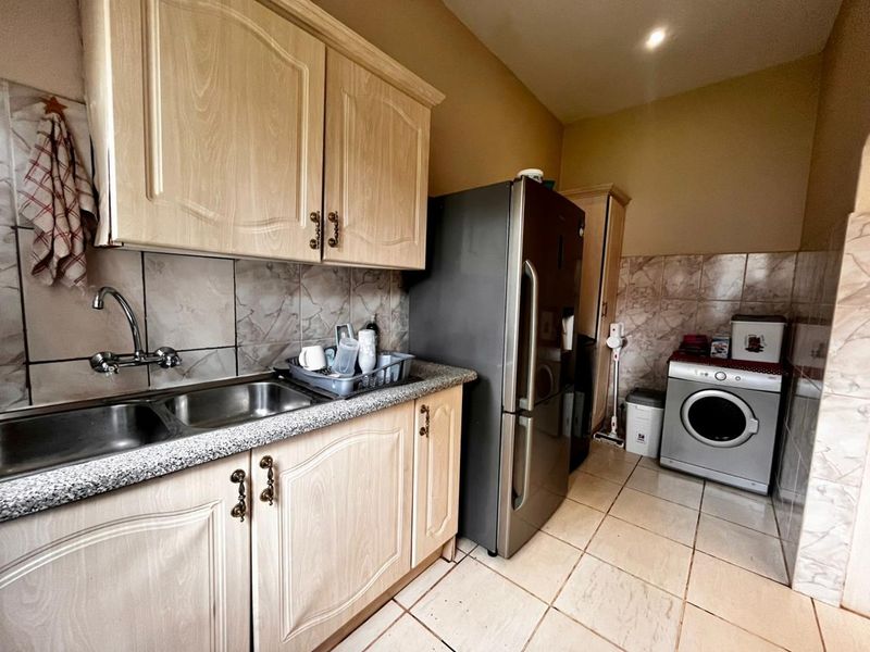 Functional kitchen featuring light wood-finish cabinetry, granite-look laminate countertops, tiled splashbacks, and integrated space for laundry appliances.