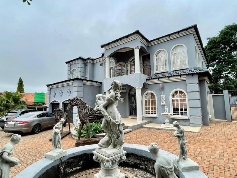 Front elevation of a two-story house featuring a paved driveway, double garage, arched windows, and a decorative fountain in the foreground.