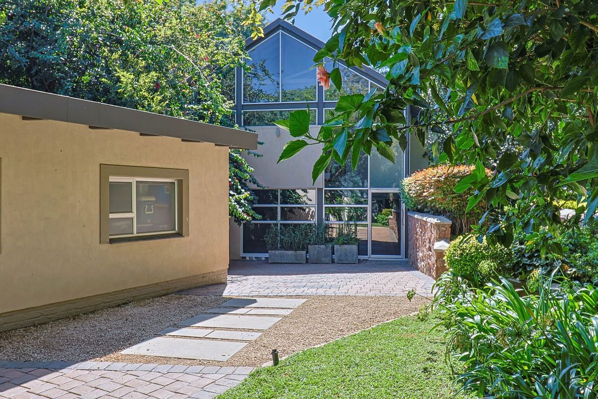 A well-maintained rear exterior featuring a paved patio, stone retaining wall, and a striking modern glass facade overlooking a landscaped garden.