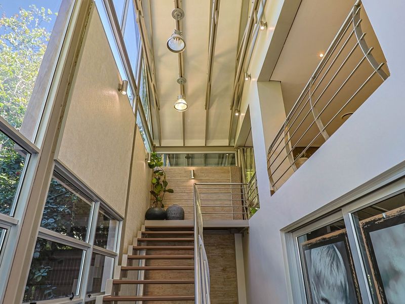 A bright, double-volume entrance hallway featuring a modern staircase, metal balustrades, and expansive clerestory windows that provide abundant natural light.