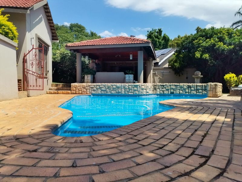 Outdoor pool area featuring a paved deck, stone-clad water feature, and a covered patio space, ideal for relaxation and entertainment.