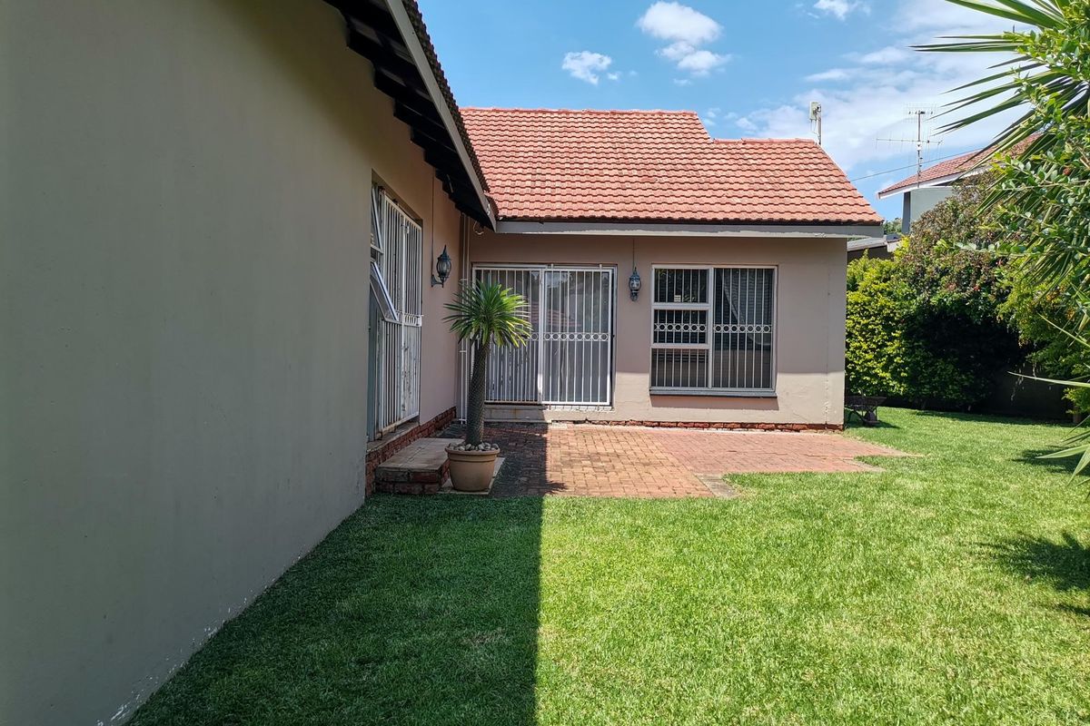 Rear view of the property featuring a brick paved patio area, well-maintained lawn, and secure sliding door access to the home.