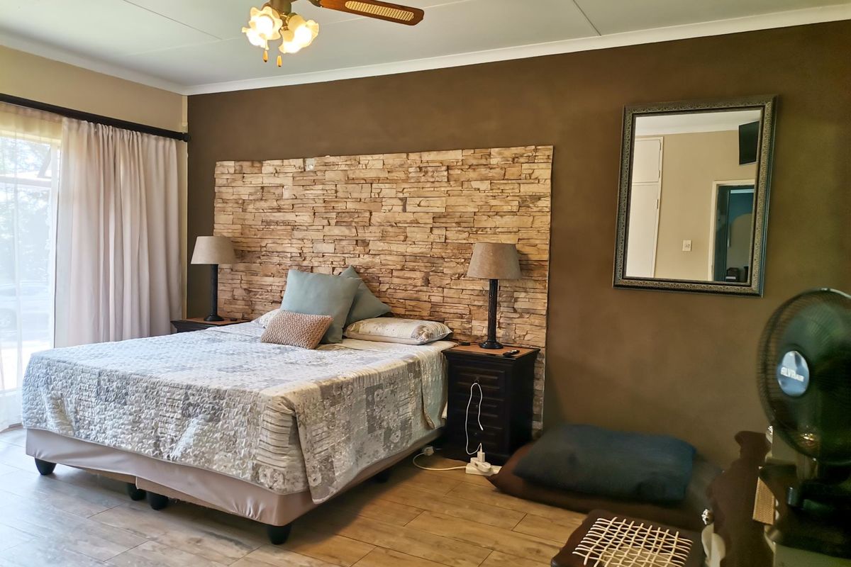 Spacious bedroom featuring a stone accent wall, tiled flooring, ceiling fan, and direct access to the outdoors via a sliding glass door.