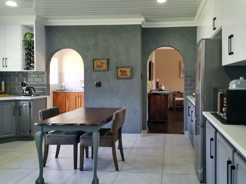 A modern kitchen featuring grey cabinetry, subway tile backsplash, and distinctive archways leading to adjacent living spaces, finished with tiled flooring.