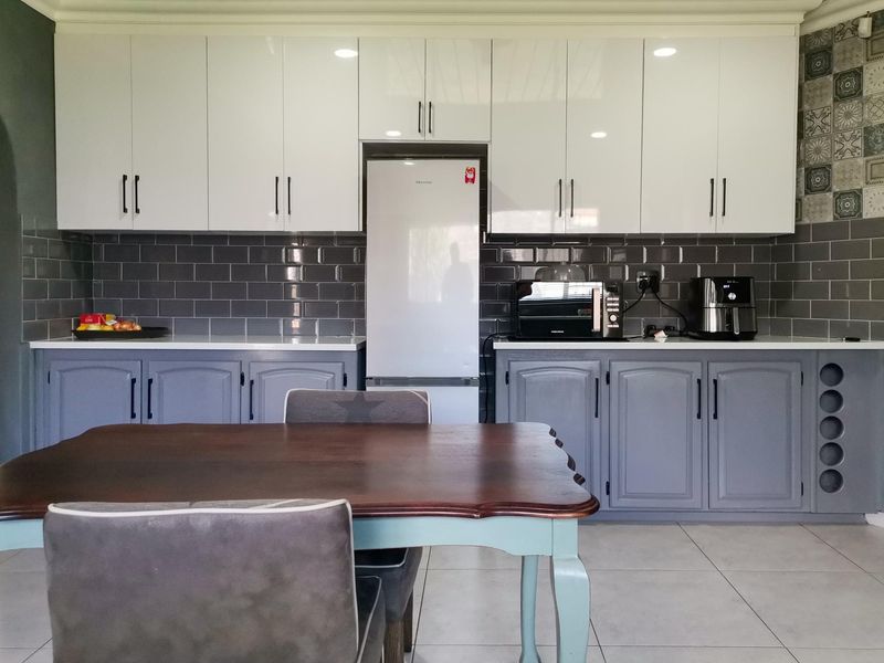 Modern kitchen featuring white upper cabinets, grey lower cabinetry, subway tile backsplash, and stone countertops with integrated storage and wine rack.