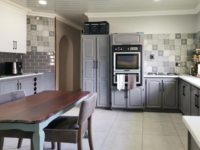 A functional kitchen featuring built-in cabinetry, a double oven, gas hob, and decorative tiled backsplash with neutral floor tiles.