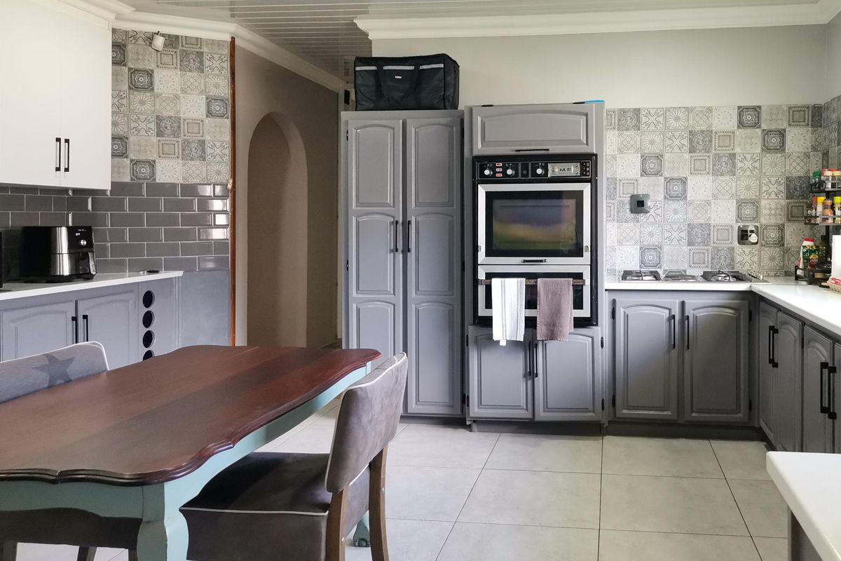 A functional kitchen featuring built-in cabinetry, a double oven, gas hob, and decorative tiled backsplash with neutral floor tiles.