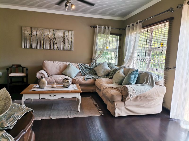 A comfortable living room featuring dark timber-look flooring, a tongue and groove ceiling with a fan, and large windows with security bars.