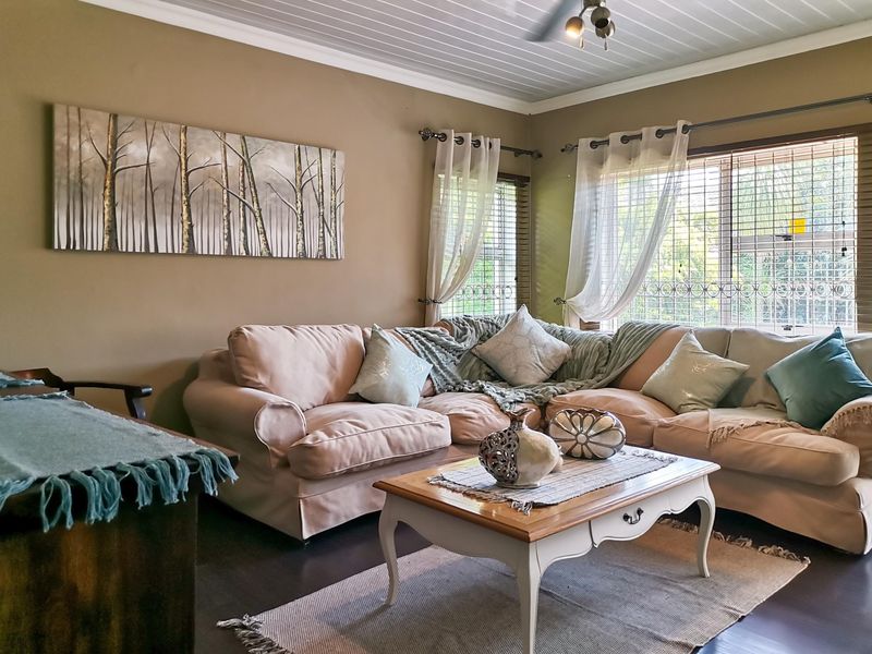 A comfortable living room featuring timber-look flooring, a tongue and groove ceiling, and large windows fitted with security bars.