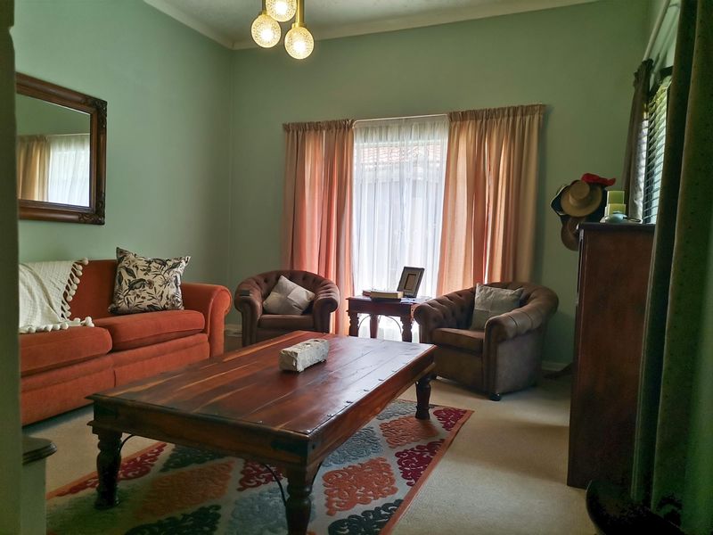 A comfortable living room featuring soft green walls, natural light through window curtains, and a central ceiling light fixture.