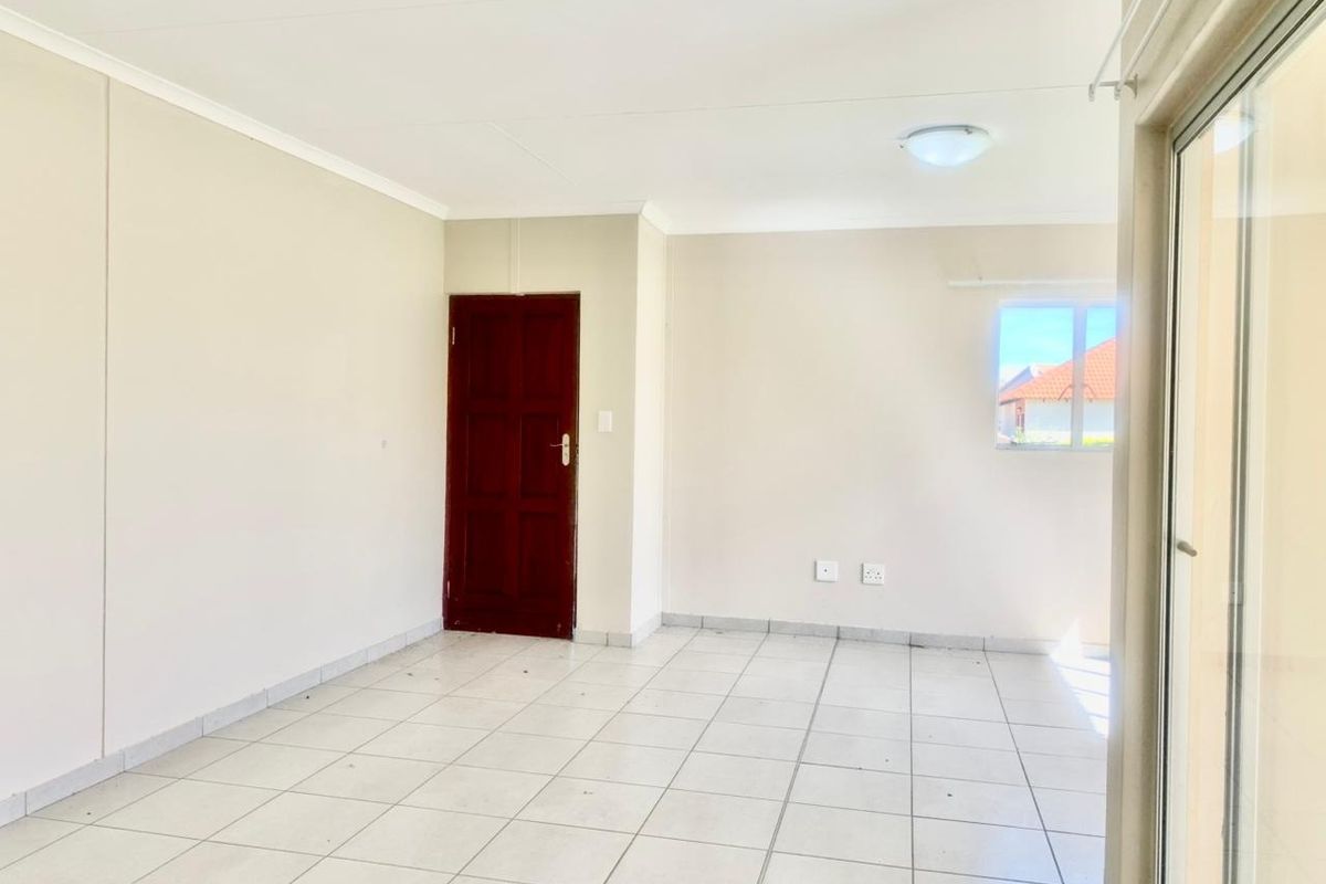 A bright, empty living area featuring neutral walls, tiled flooring, and a sliding glass door providing access to the exterior.