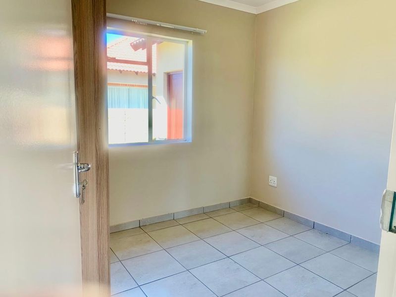 A clean, empty bedroom featuring neutral wall paint, tiled flooring, and an aluminium-framed window, providing a blank canvas for personalization.