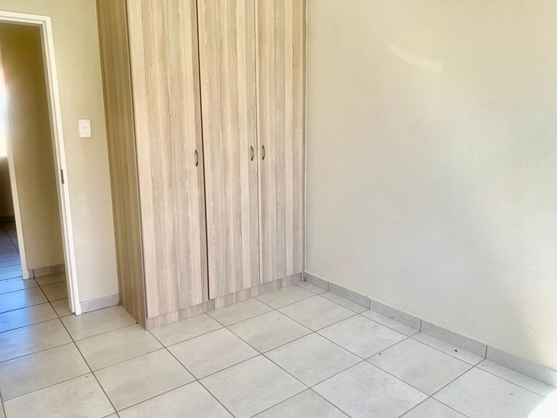 A clean, empty bedroom featuring neutral tiled flooring and modern light wood-finish built-in cupboards.