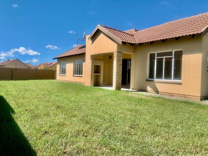 Rear view of the house featuring a tiled roof, brick facade, covered patio with a built-in braai, and a spacious lawn area.