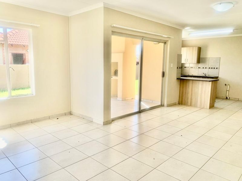 An open-plan living and kitchen area featuring neutral tiled flooring, built-in cabinetry, and a sliding glass door leading to an outdoor patio space.
