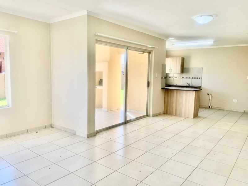 An open-plan living and kitchen area featuring tiled flooring, neutral walls, and a sliding glass door leading to an outdoor patio space.