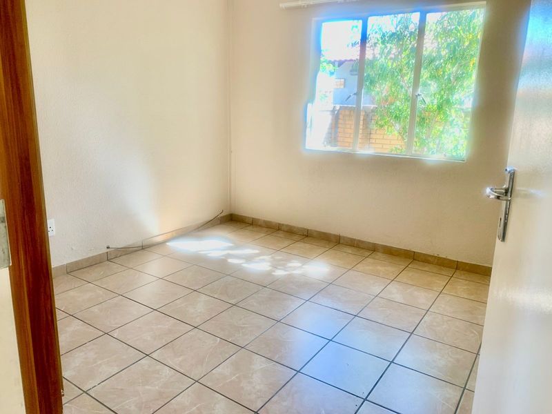 A vacant bedroom featuring neutral tiled flooring, a large window providing natural light, and standard finishes, ready for personalization.