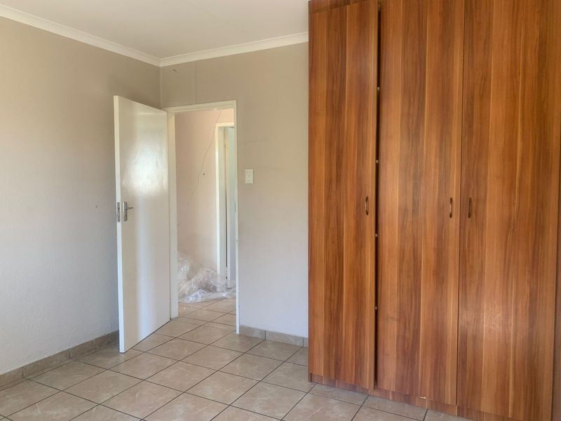 A bedroom featuring tiled flooring and a large built-in wooden wardrobe, with a visible wall crack requiring attention.