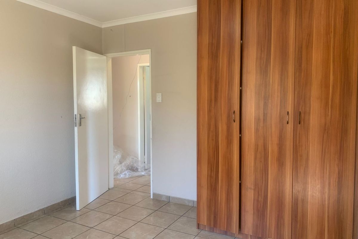 A bedroom featuring tiled flooring and a large built-in wooden wardrobe, with a visible wall crack requiring attention.