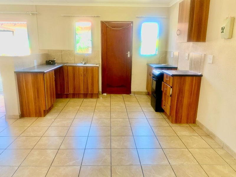 A functional kitchen featuring wood-look laminate cabinetry, tiled flooring, a stainless steel sink, and a freestanding stove, offering a clean and practical workspace.