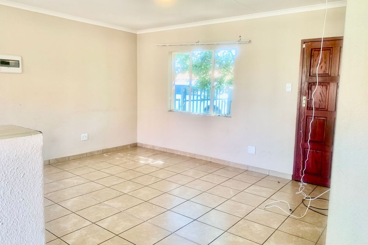 An empty living room featuring neutral walls, tiled flooring, and a wooden door, providing a blank canvas for interior design.