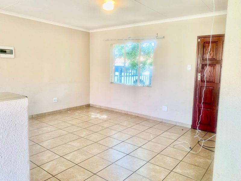 An empty living room featuring neutral walls, tiled flooring, and a wooden door, providing a blank canvas for interior design.