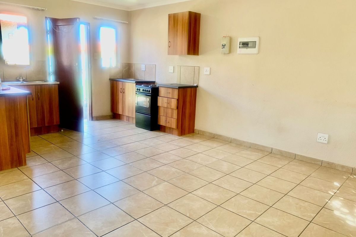 A functional, open-plan kitchen featuring tiled flooring, wood-finish cabinetry, laminate countertops, and a freestanding stove with direct access to the exterior.