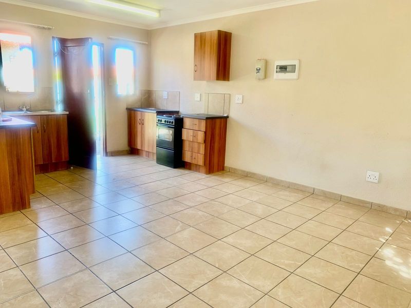 A functional, open-plan kitchen featuring tiled flooring, wood-finish cabinetry, laminate countertops, and a freestanding stove with direct access to the exterior.