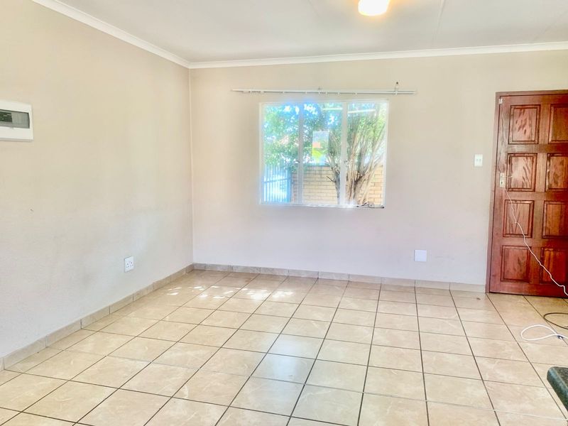 A vacant living area featuring neutral tiled flooring, a timber panel door, and natural light through an aluminium-framed window.