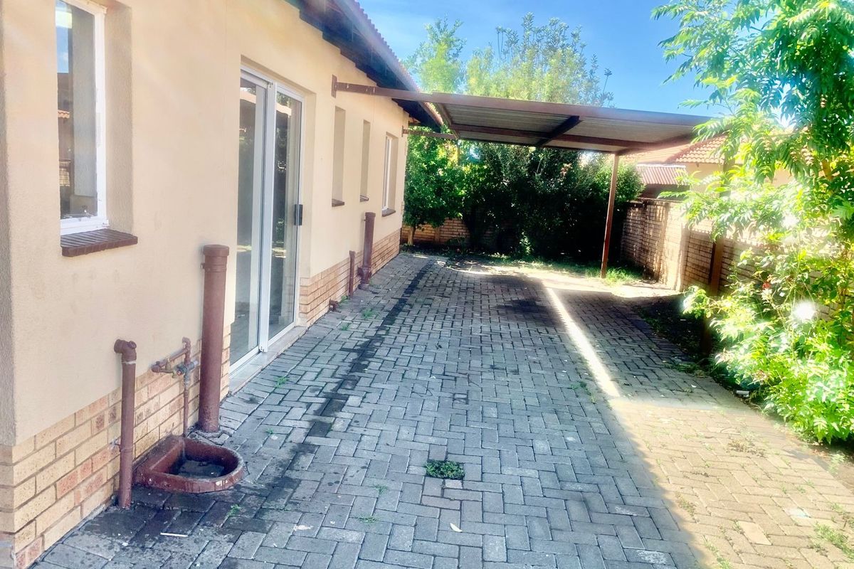 Rear exterior view featuring a paved driveway, a covered carport, and sliding glass door access to the main dwelling.