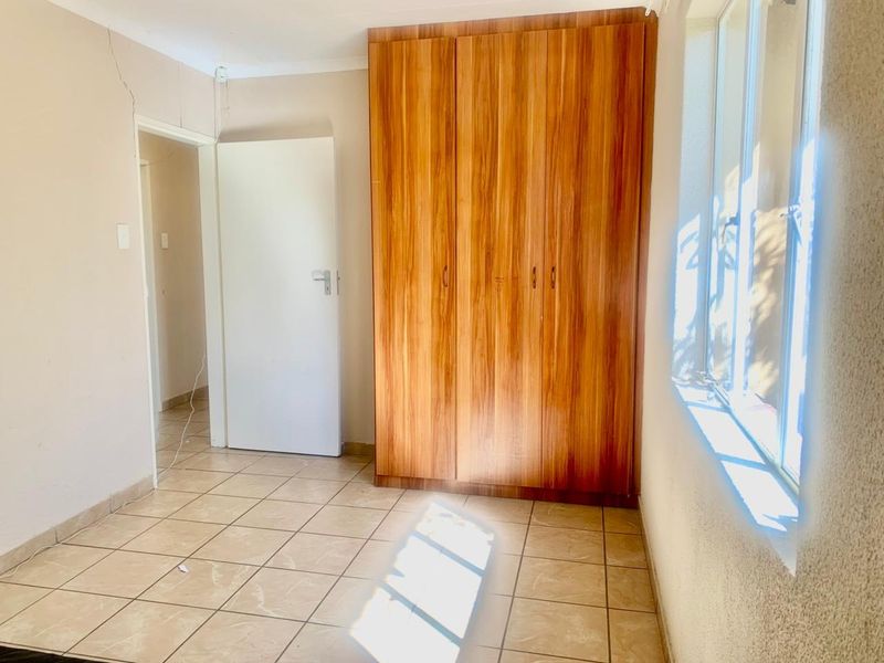An empty bedroom featuring tiled flooring and built-in wooden cupboards, with a visible wall crack requiring attention.