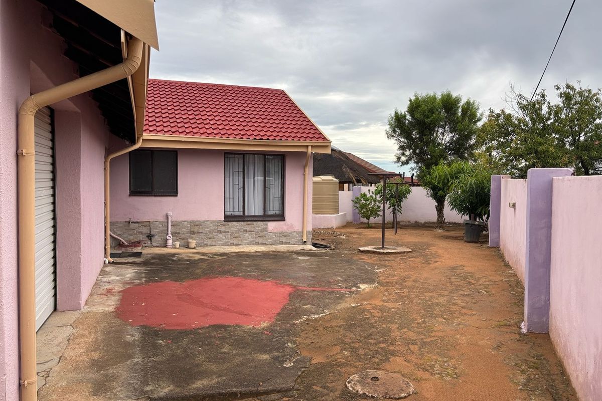 Rear exterior view of the property featuring a red tiled roof, concrete apron, perimeter wall, and a water tank in a modest garden setting.