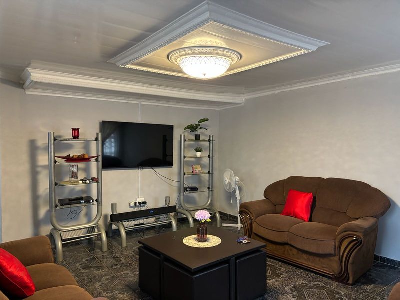 A living room featuring tiled flooring, decorative crown molding, and an ornate ceiling rose with a central light fixture.