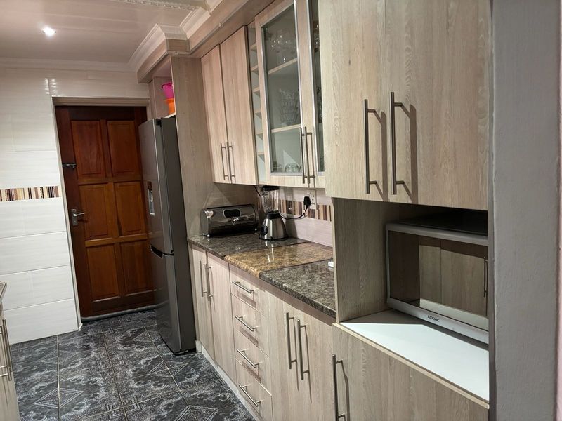 A functional kitchen featuring light wood-grain cabinetry, granite countertops, tiled backsplash, and dark patterned floor tiles.