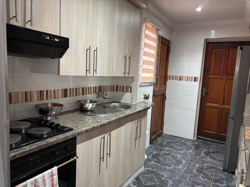 A functional kitchen featuring light wood-grain cabinetry, granite-look laminate countertops, a built-in electric oven and hob, and durable tiled flooring.