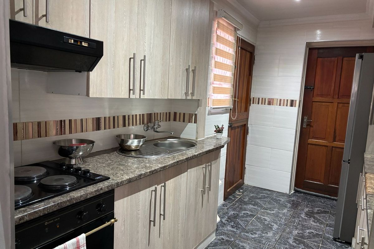 A functional kitchen featuring light wood-grain cabinetry, granite-look laminate countertops, a built-in electric oven and hob, and durable tiled flooring.