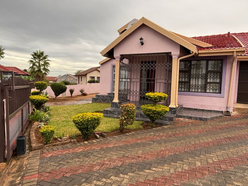 Front view of a residential house featuring a paved driveway, landscaped garden, covered entrance with security gate, and tiled roof.