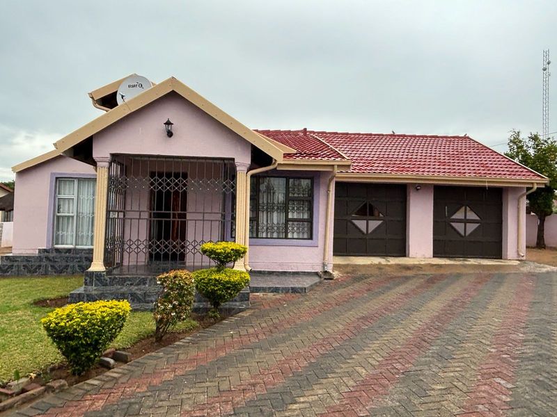 Front view of a single-story house featuring a tiled roof, double garage, paved driveway, and a covered entrance porch with security gates.